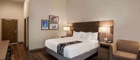 A hotel room with a large bed, bedside tables, a chair, and artwork on the wall.