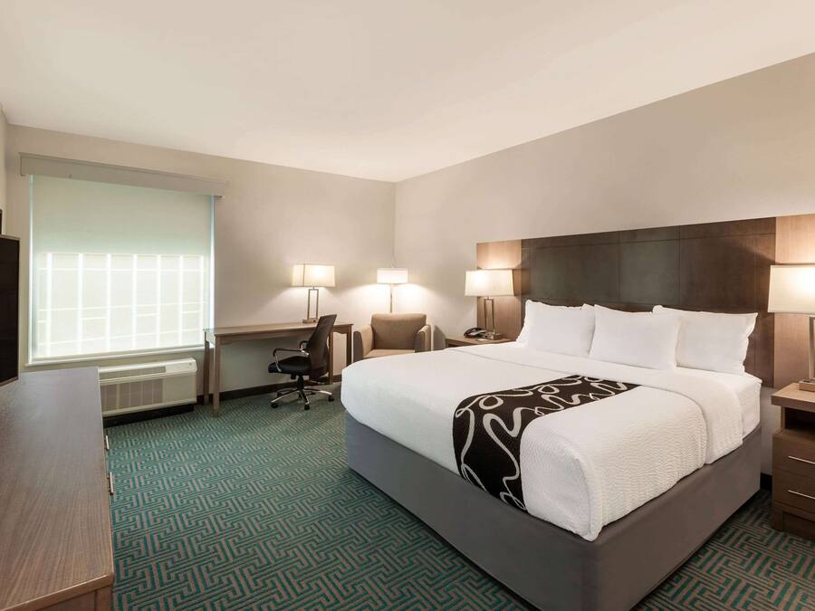 A hotel room with a large bed, a desk, a chair, and a window with blinds.