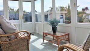 A conservatory with wicker furniture, a glass table, and a view of the outside. - Meadow View Apartments (Newquay)