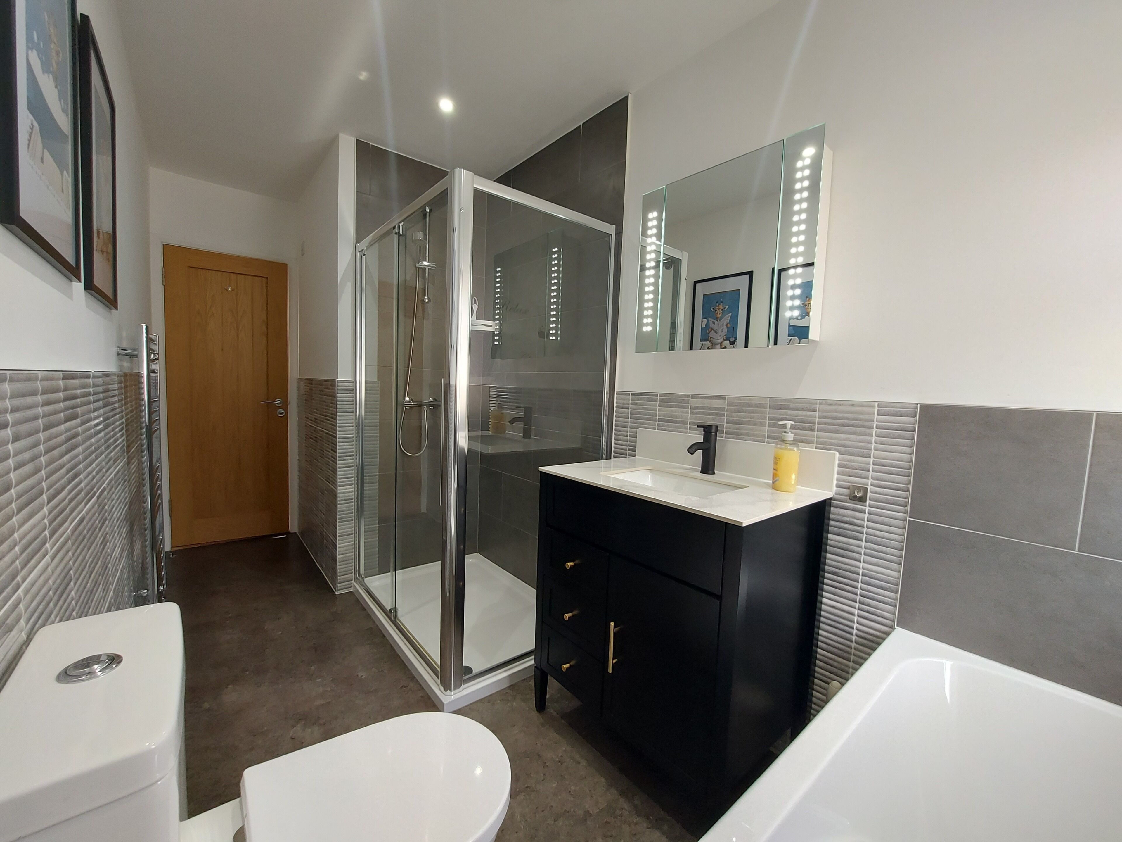 Een moderne badkamer met een douchecabine van glas, een wit toilet, een zwart wastafelmeubel met spiegel en een bad.
