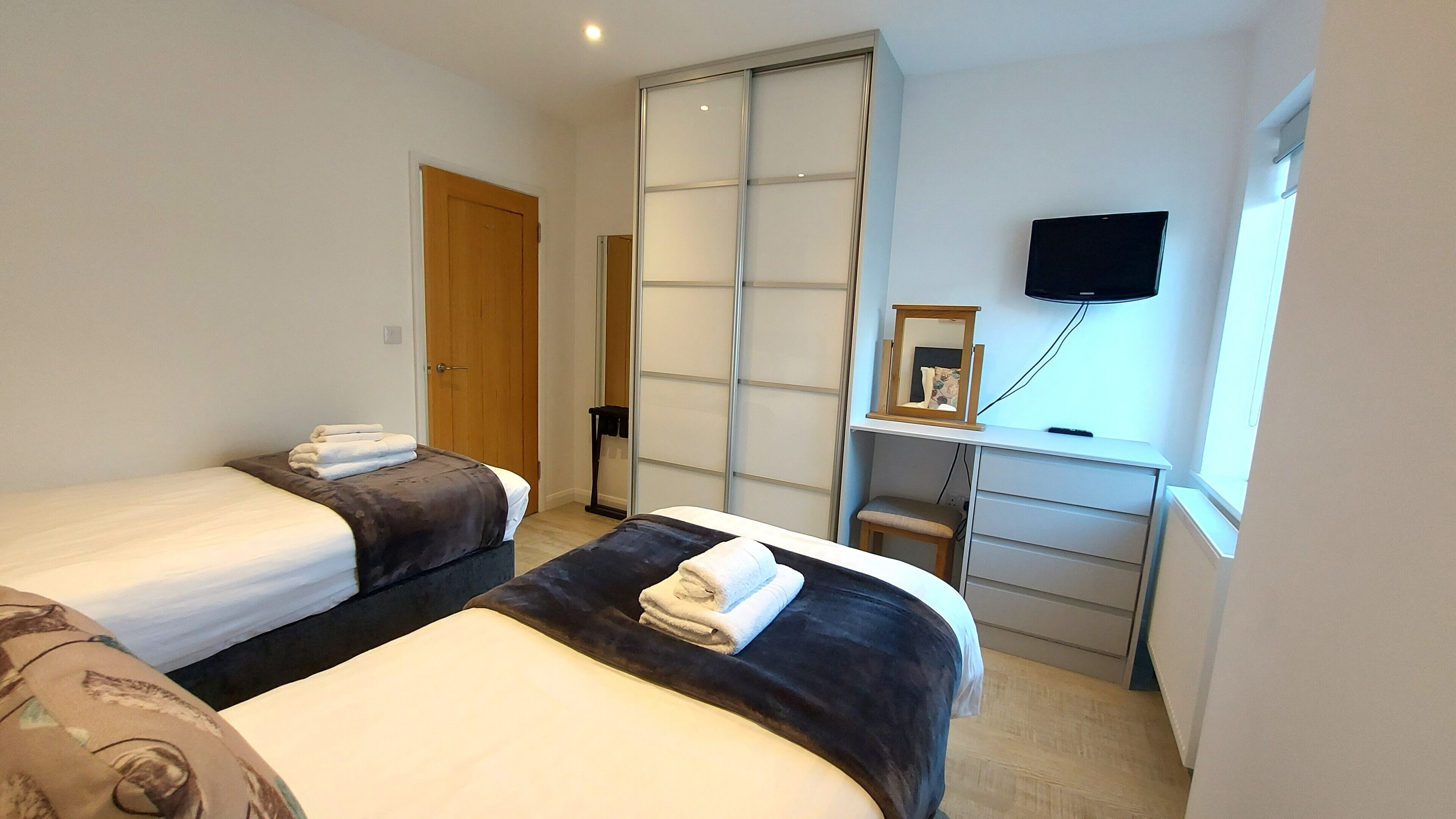 Habitación de hotel con dos camas, un escritorio con televisor, una puerta corredera y una ventana.
