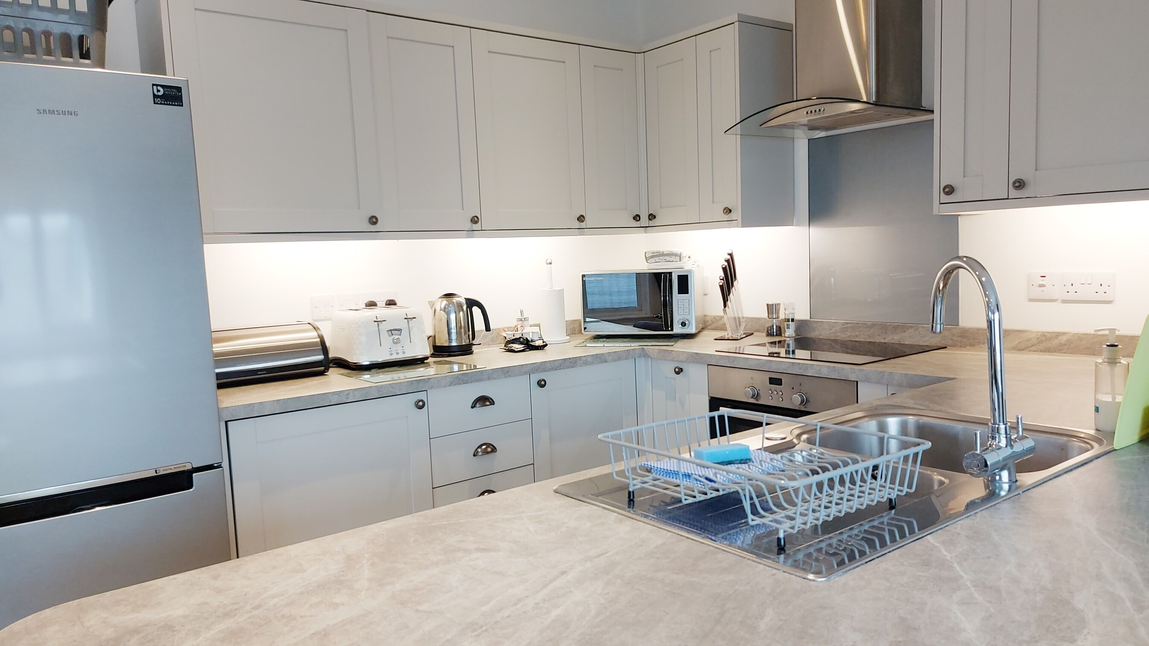 A modern kitchen with white cabinets, stainless steel appliances, a dishwasher, and a sink with a dish rack.