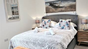 Una cama bien hecha con una colcha estampada, dos lámparas de noche y un cuadro de un barco en la pared.