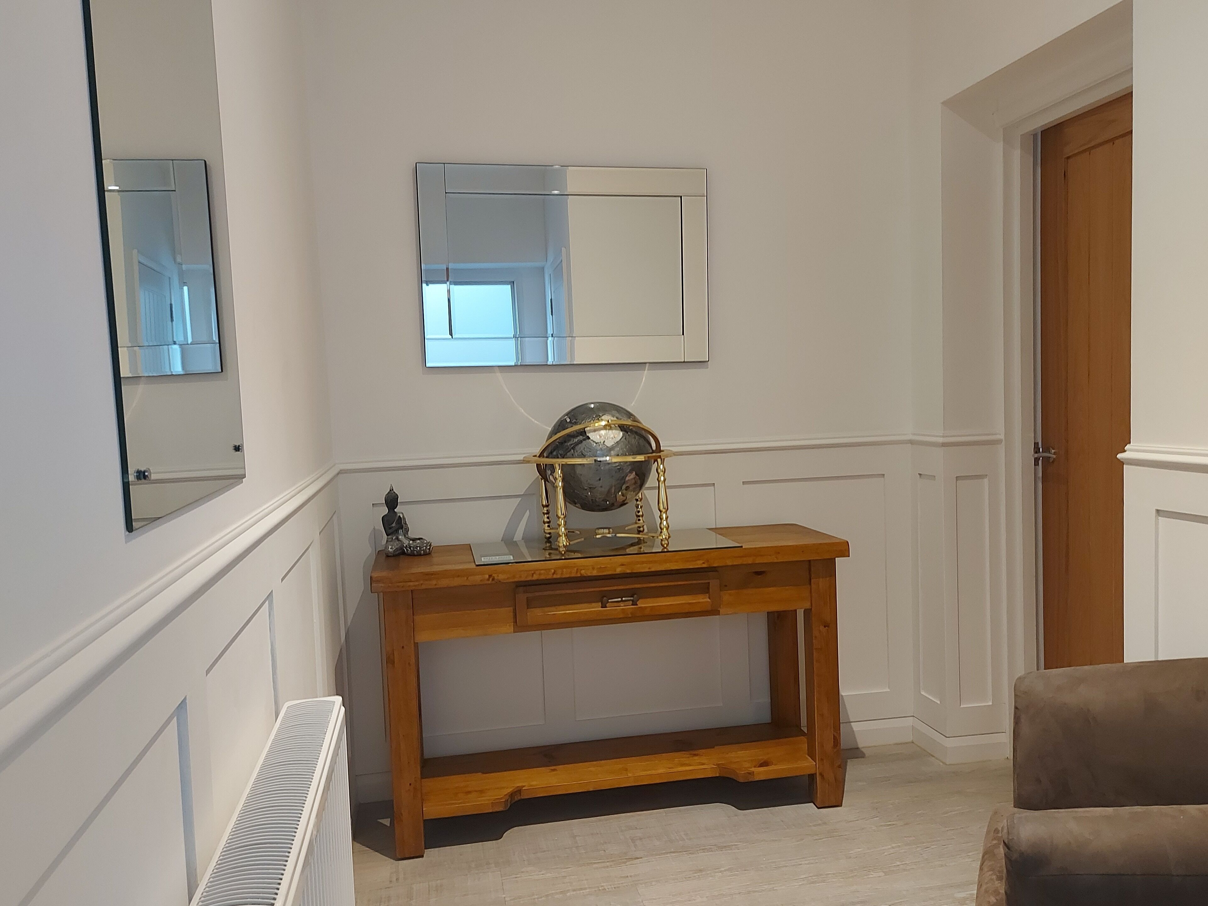 A wooden desk with a globe and a statue, a mirror on the wall, and a radiator.