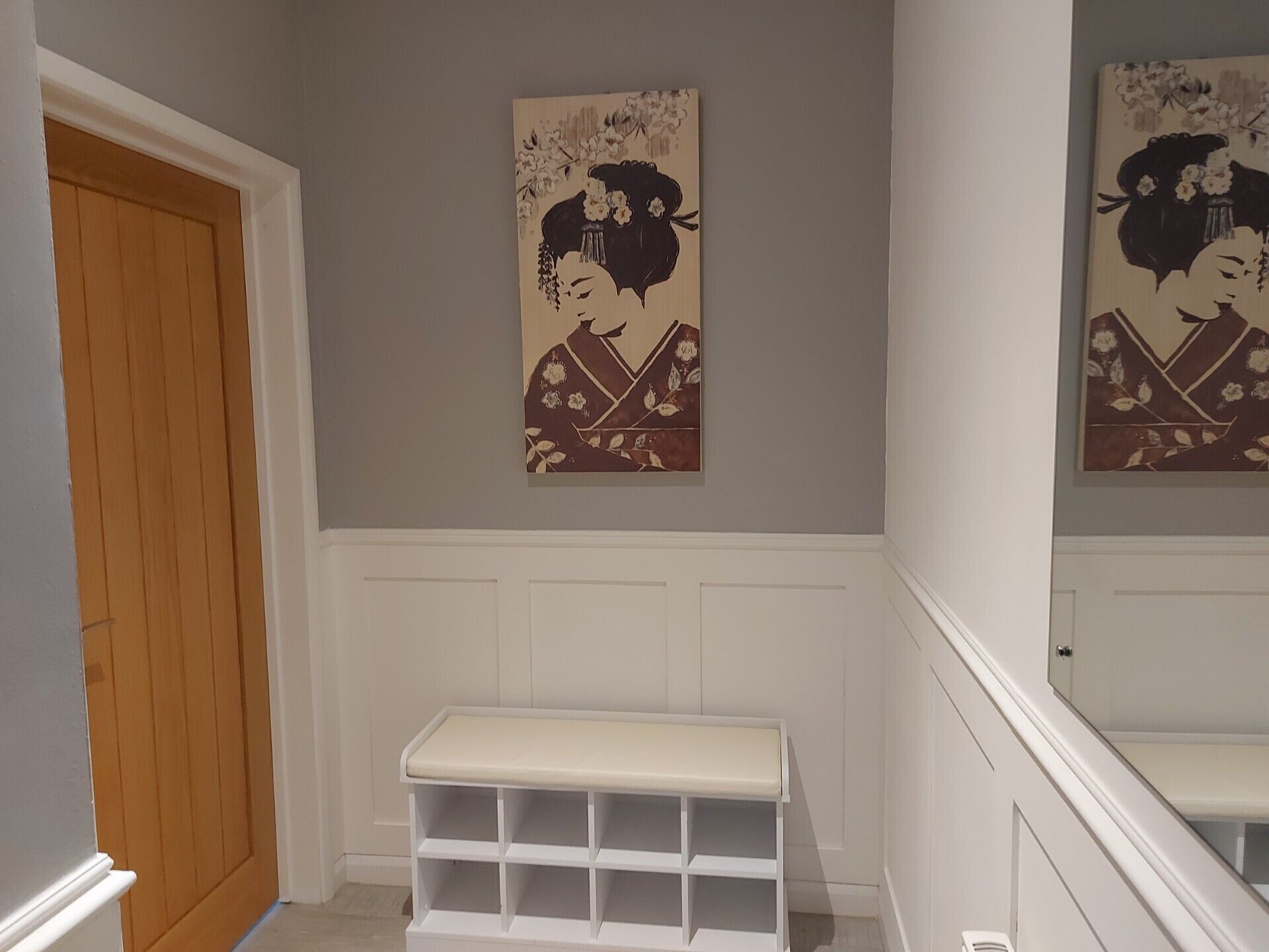 A hallway with a wooden door, a white bench, and two wall-mounted artworks depicting a figure in traditional attire.
