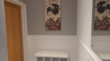 A hallway with a wooden door, a white bench, and two wall-mounted artworks depicting a figure in traditional attire.