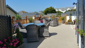 An outdoor patio with wicker furniture and a table, surrounded by a wooden fence and potted plants. - Meadow View Apartments (Newquay)