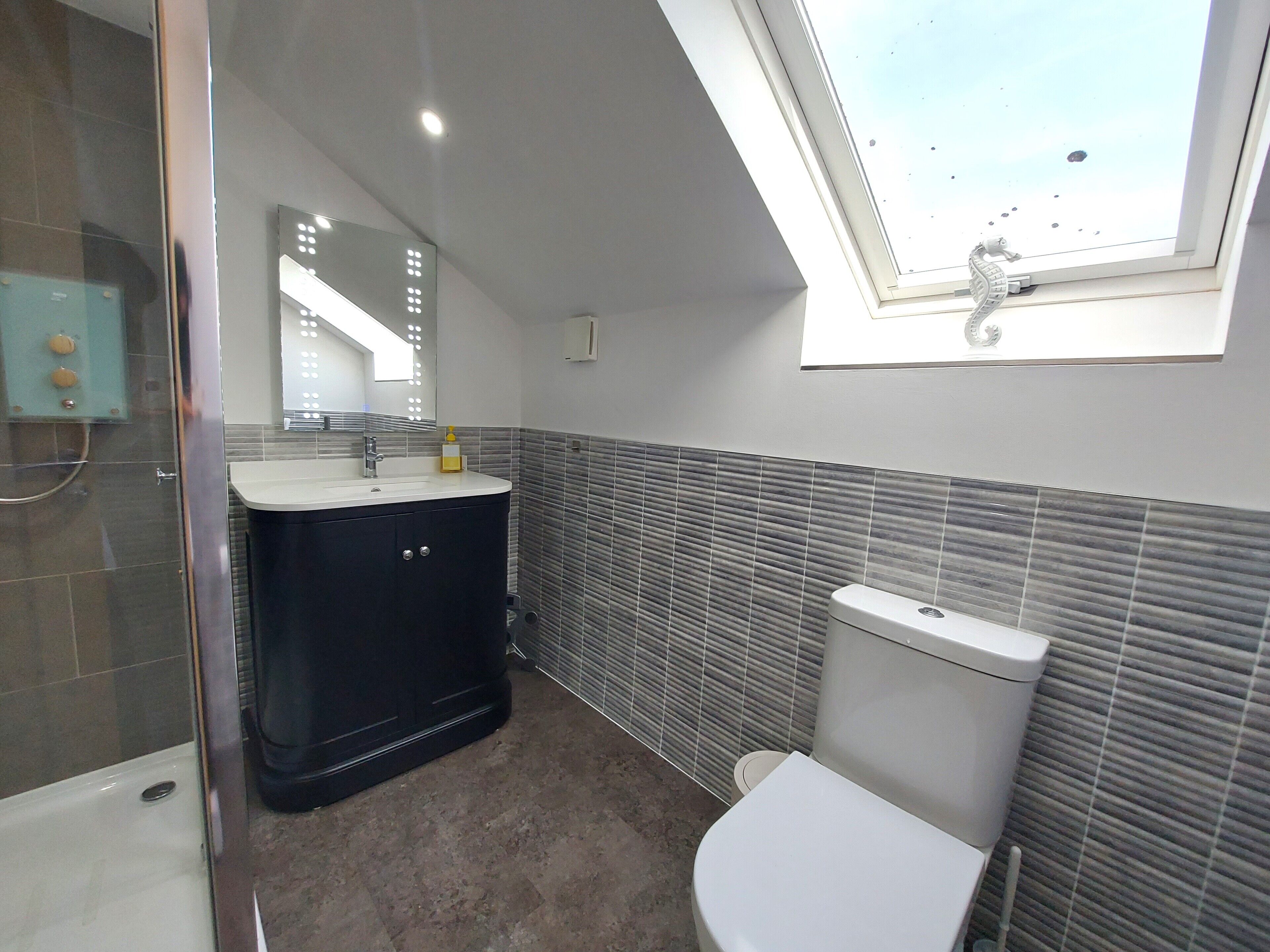 Een moderne badkamer met een douche, wastafel, toilet en dakraam.