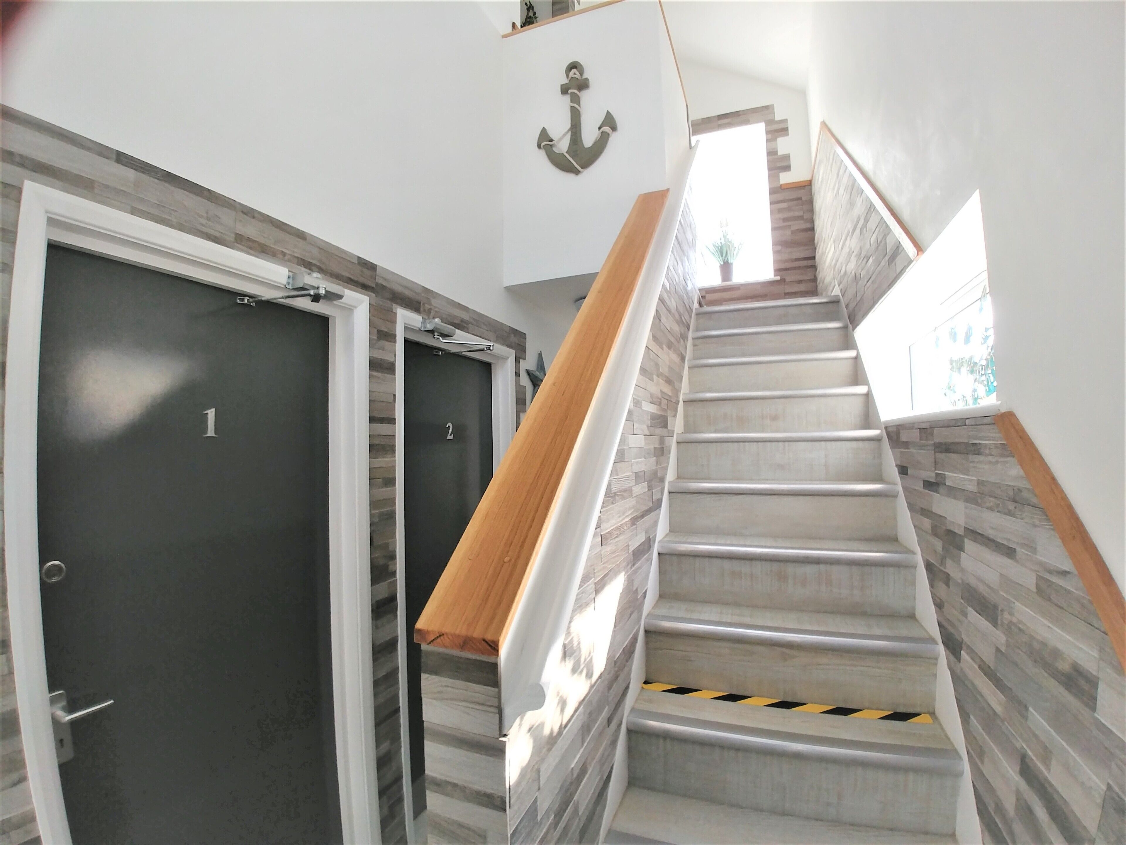 A staircase with a wooden handrail and a tiled wall. There are two doors with numbers 1 and 2.