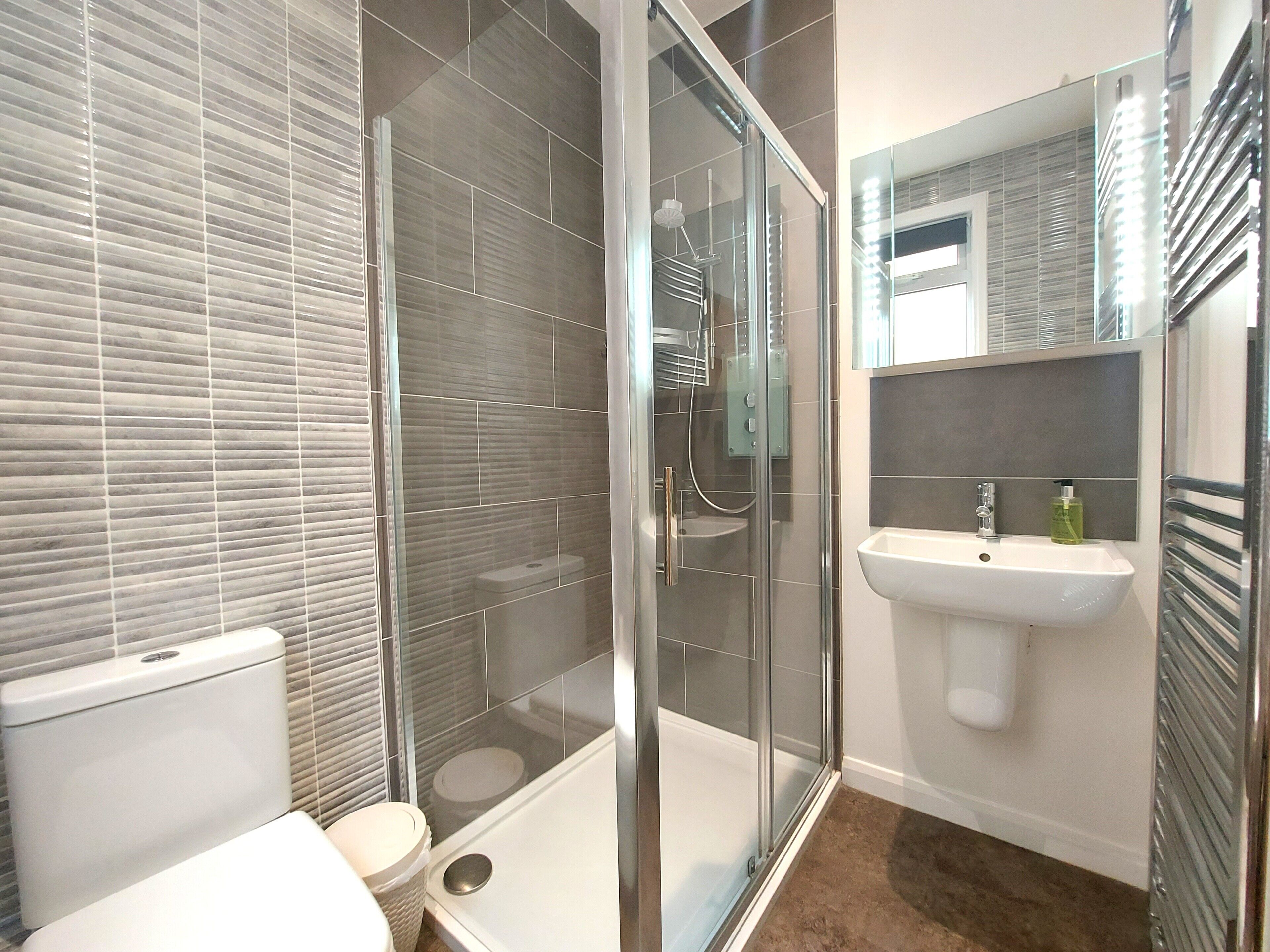 A modern bathroom with a glass shower enclosure, a white sink, and a toilet.