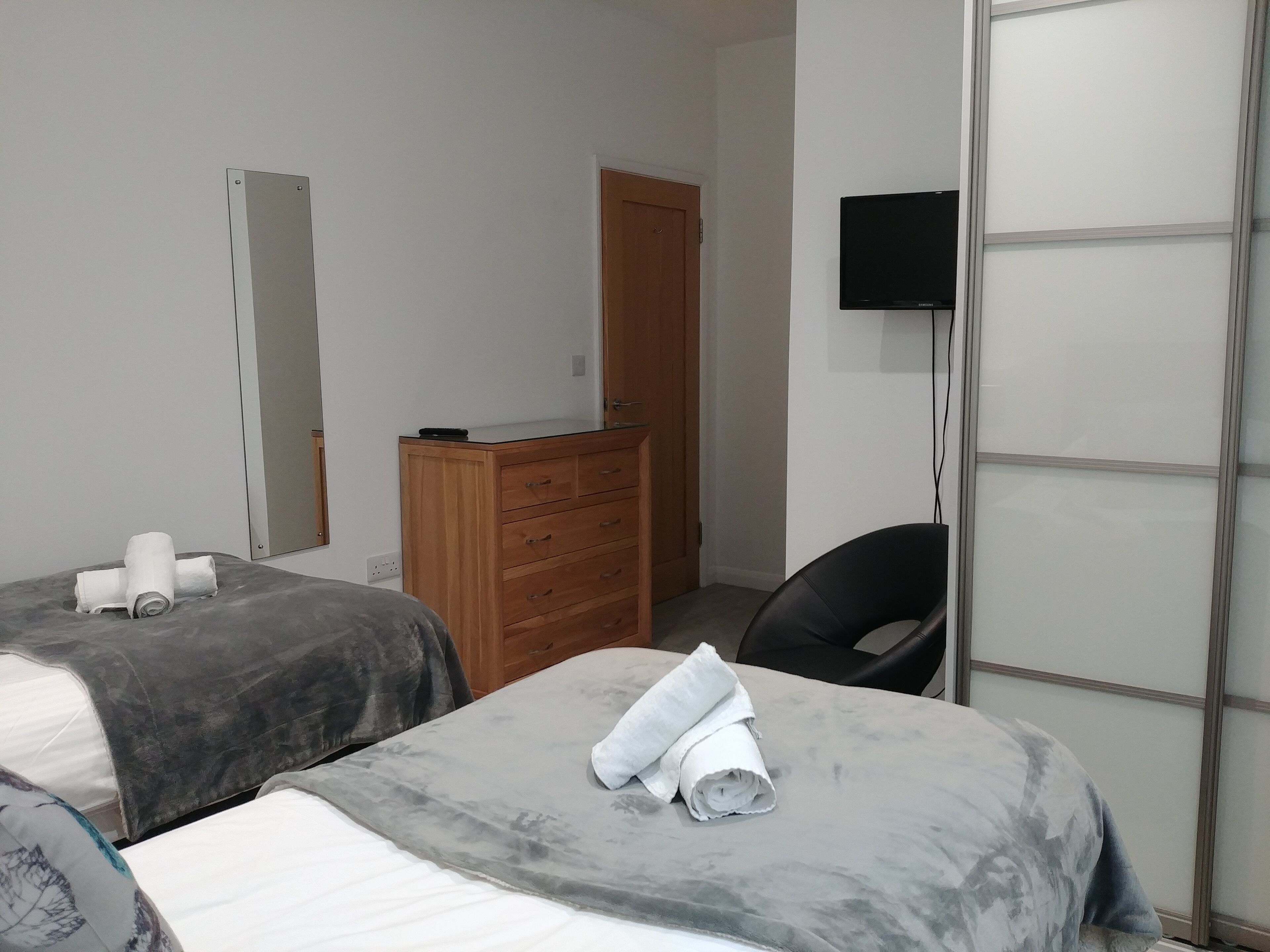 A hotel room with two beds, a wooden dresser, a television, and a door.
