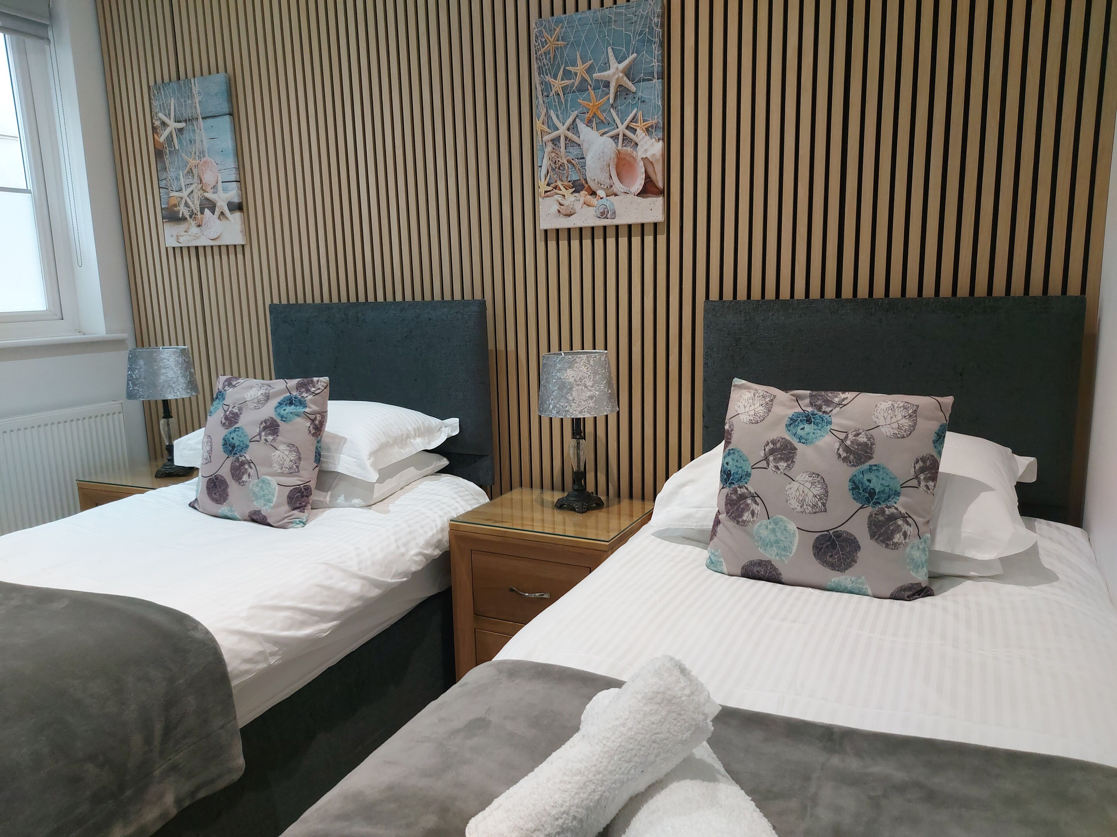 Habitación de hotel con dos camas, cada una con una almohada y una mesita de noche con lámpara.
