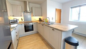 A modern kitchen with white cabinets, a built-in oven, a microwave, and a stainless steel trash bin. - Meadow View Apartments (Newquay)
