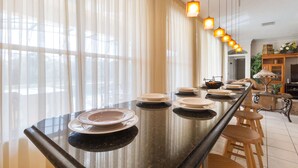 Un comedor con una mesa larga dispuesta para varias personas, que incluye una superficie reflectante y una variedad de platos y cuencos.