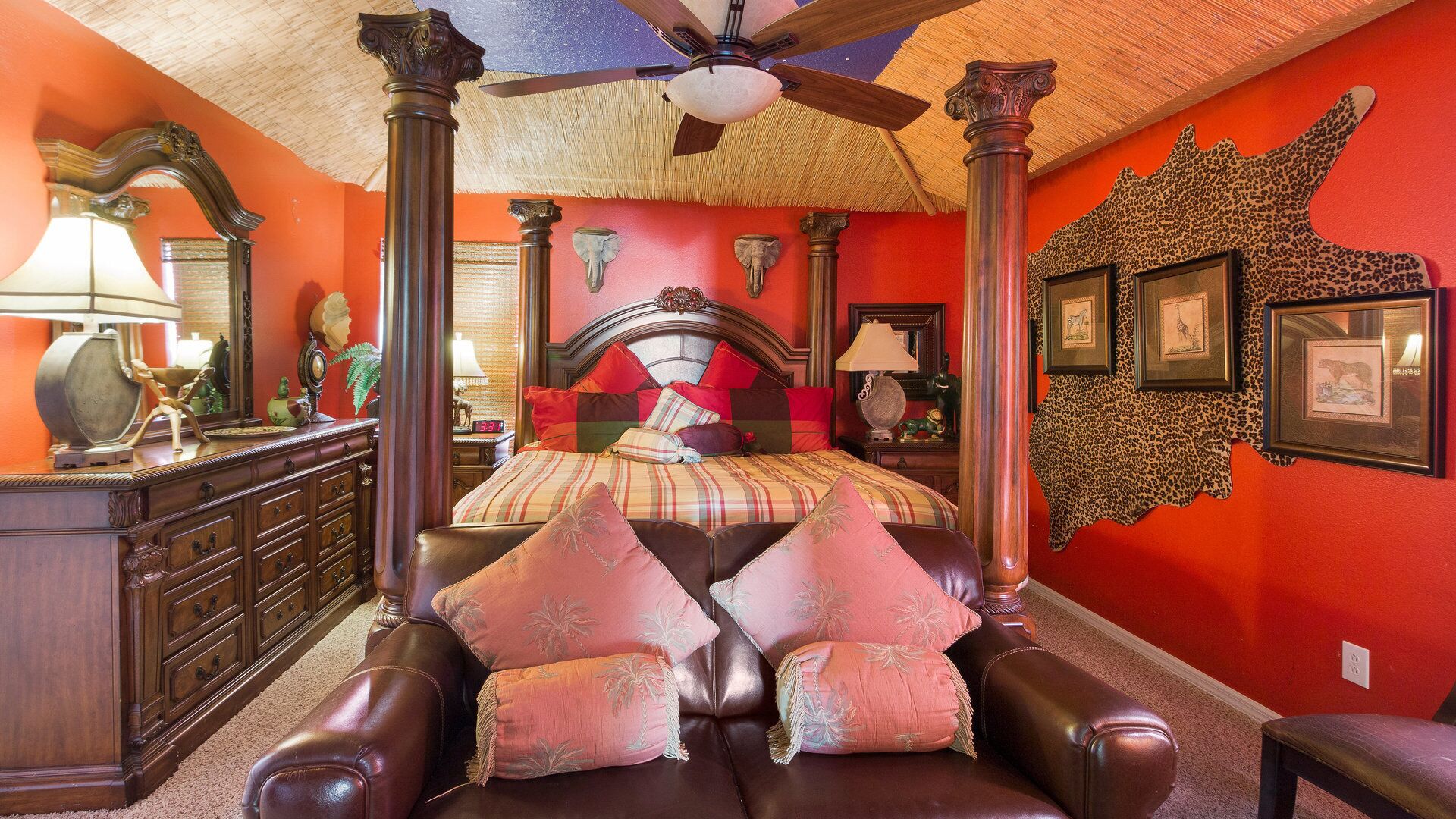 Un dormitorio con cama con dosel, ventilador de techo y pared roja decorada con estampados de animales.