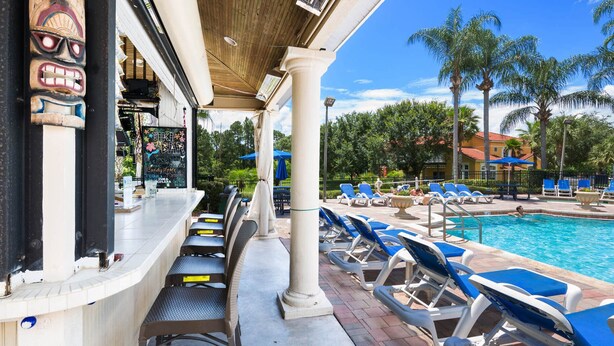 Un bar junto a la piscina con decoración tiki, sillones de descanso y una vista despejada del estanque.