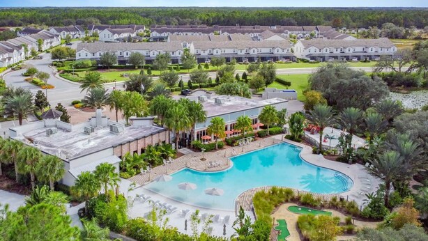 A residential area with a large swimming pool surrounded by lounge chairs and umbrellas, with houses in the background. - Enclave at Festival: Your Private Oasis of Luxury + Comfort - Davenport, Florida (Davenport)