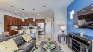 A modern living room with a leather sofa, a coffee table with a glass top, and a flat-screen TV mounted on the wall. - Enclave at Festival: Your Private Oasis of Luxury + Comfort - Davenport, Florida (Davenport)