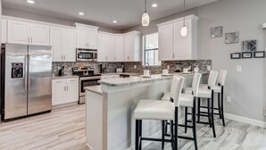 Una cocina moderna con armarios blancos, electrodomésticos de acero inoxidable y una isla central con taburetes de bar.