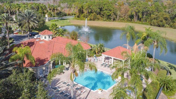 A resort with a swimming pool, lounge chairs, and a fountain.