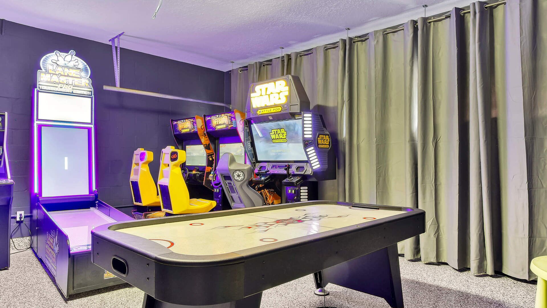 A room with a pool table, two arcade machines, and a neon sign.