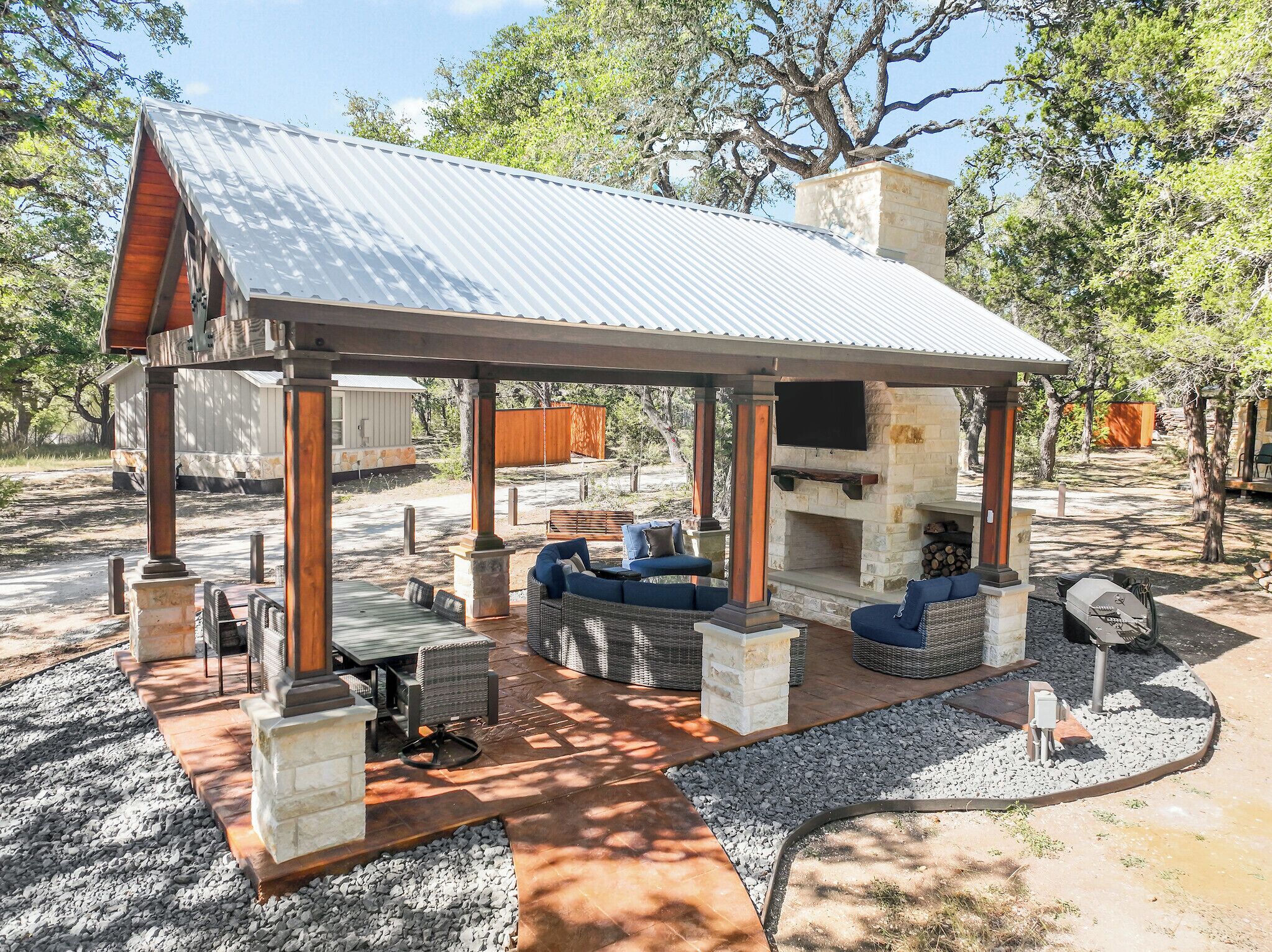 A covered outdoor patio with a stone fireplace, seating area, and grill.