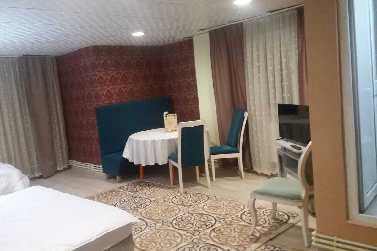 Habitación de hotel con dos camas, una mesita con sillas, televisión y alfombras estampadas.