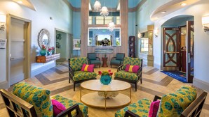 Un hall d’entrée spacieux, doté d’une table ronde centrale, de deux fauteuils et d’un canapé, le tout recouvert d’un tissu aux motifs tropicaux.