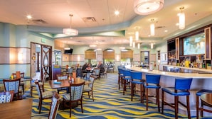 Un hall d’hôtel comprenant un bar, des espaces aménagés pour s’asseoir et un tapis à motifs.