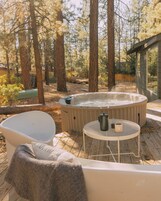 Un jacuzzi rodeado de árboles, una silla blanca y una mesita con una taza y un termo.