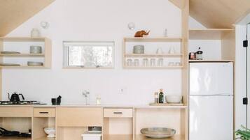 A modern kitchen with wooden shelves, a white refrigerator, and a window.
