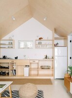 A modern kitchen with wooden shelves, a white refrigerator, and a window.