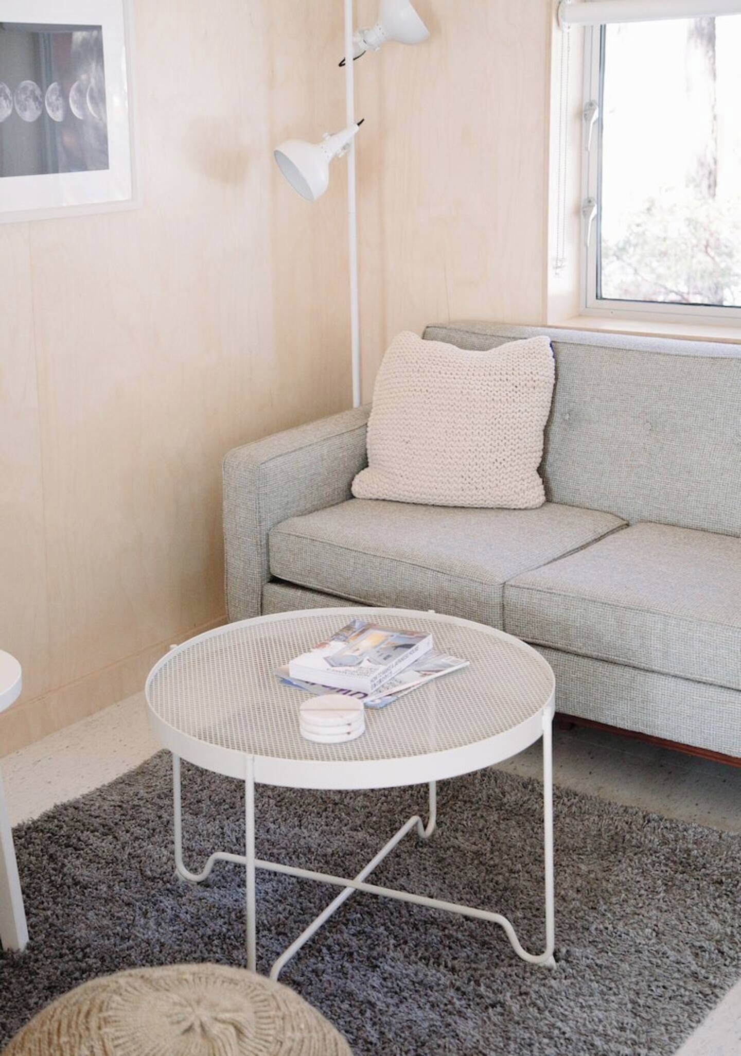 A cozy living area with a grey sofa, a round white coffee table with magazines, a grey rug, and a white lamp.