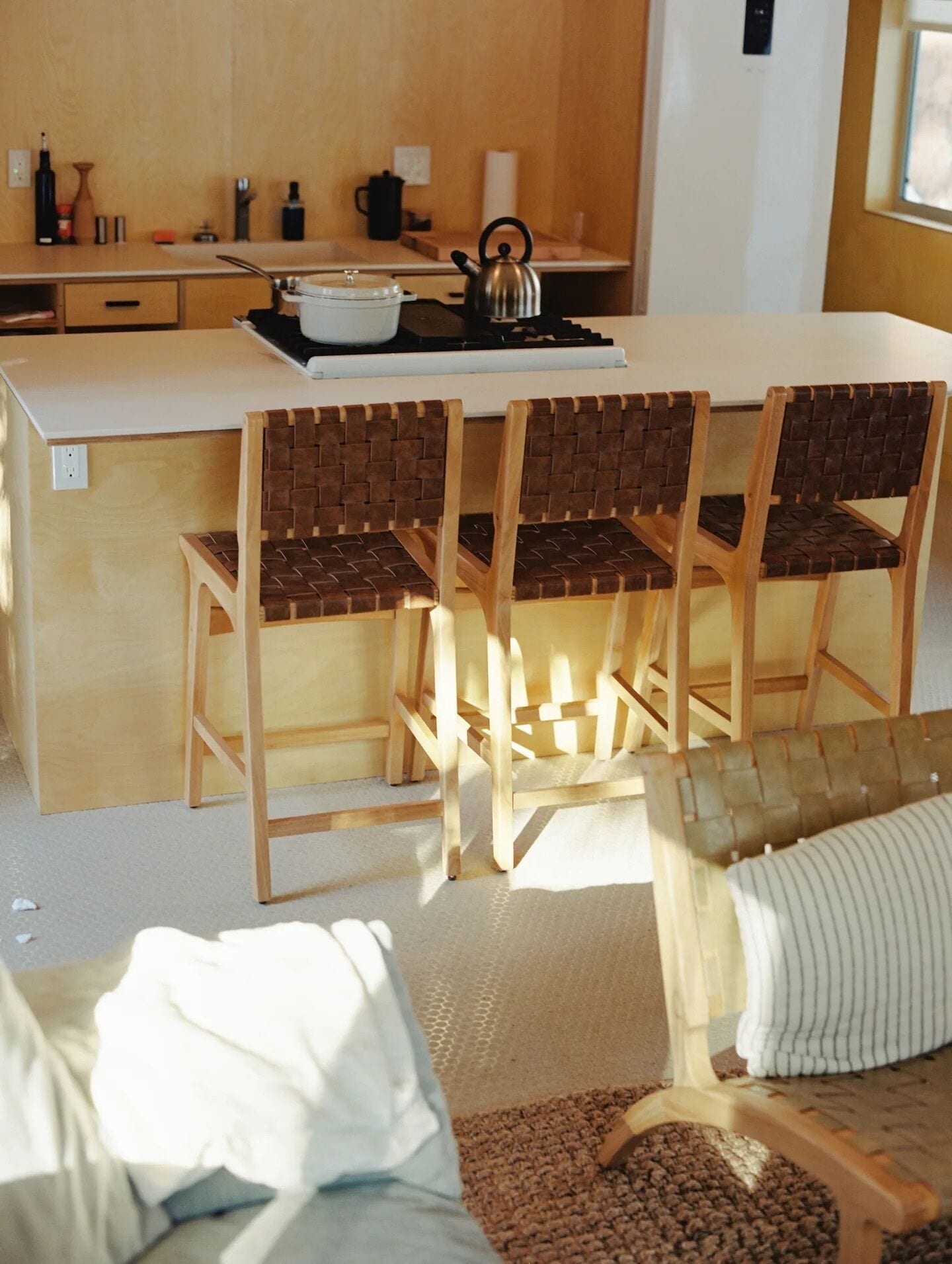 Una cocina moderna con una isla central, sillas de madera con asientos de mimbre y un comedor con cojín a rayas.