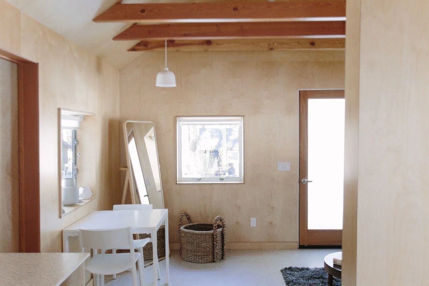 A room with a white table, chairs, a mirror, a window, and a door.