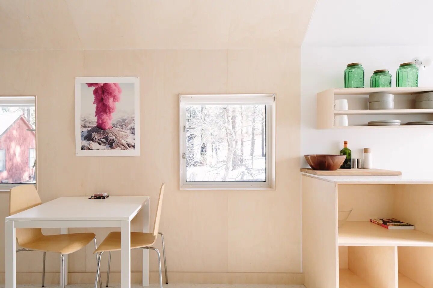 A modern kitchen with a white table and chairs, a window with a snowy view, and a shelf with jars.