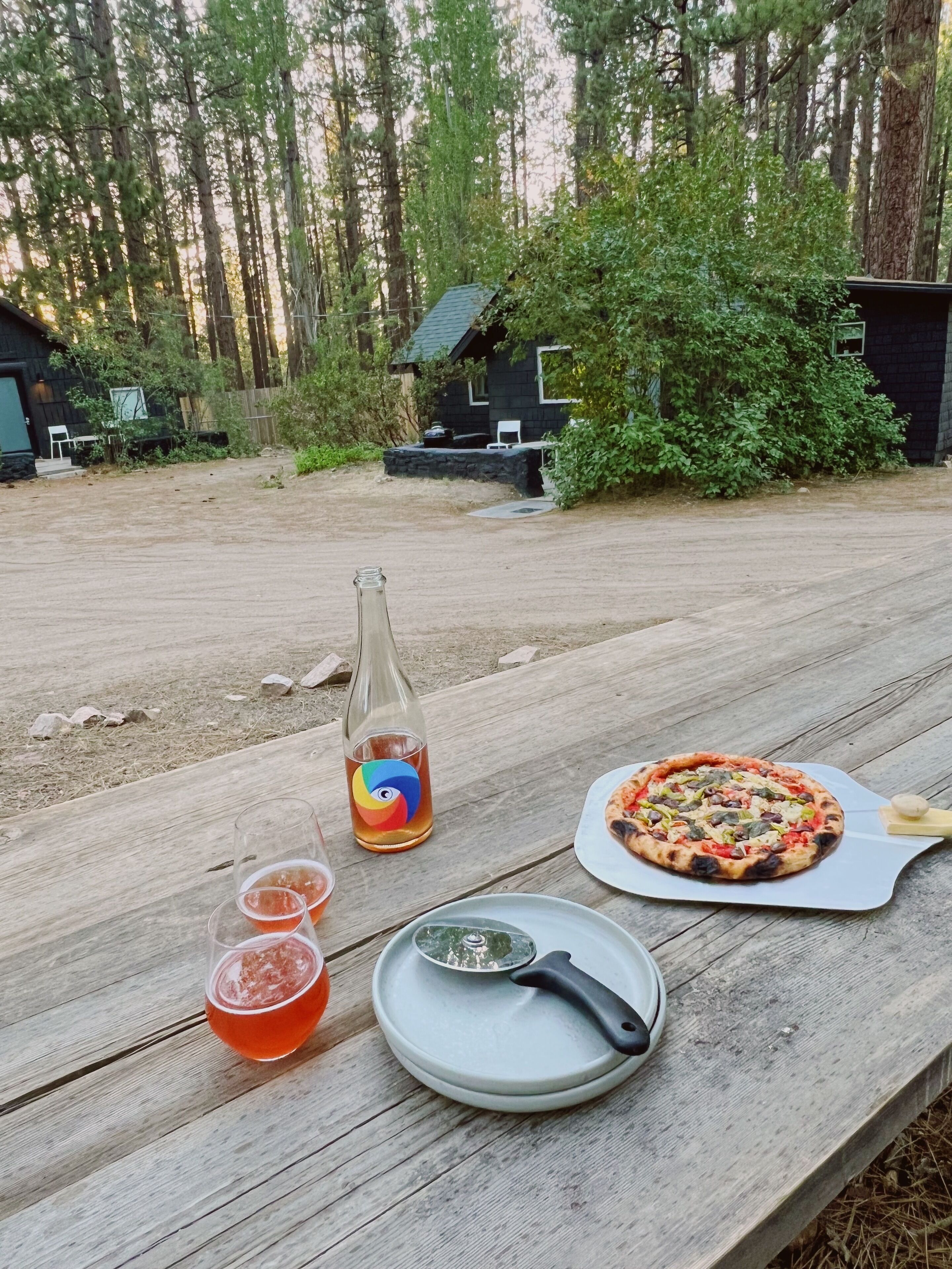 A wooden table with a pizza, a bottle, and glasses.