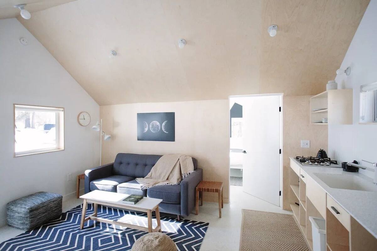 A compact living space with a sofa, a coffee table, a rug, a kitchenette, and a door leading to another room.