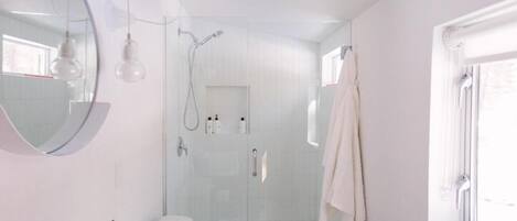 A modern bathroom with a glass-enclosed shower, a round mirror, and a white sink.