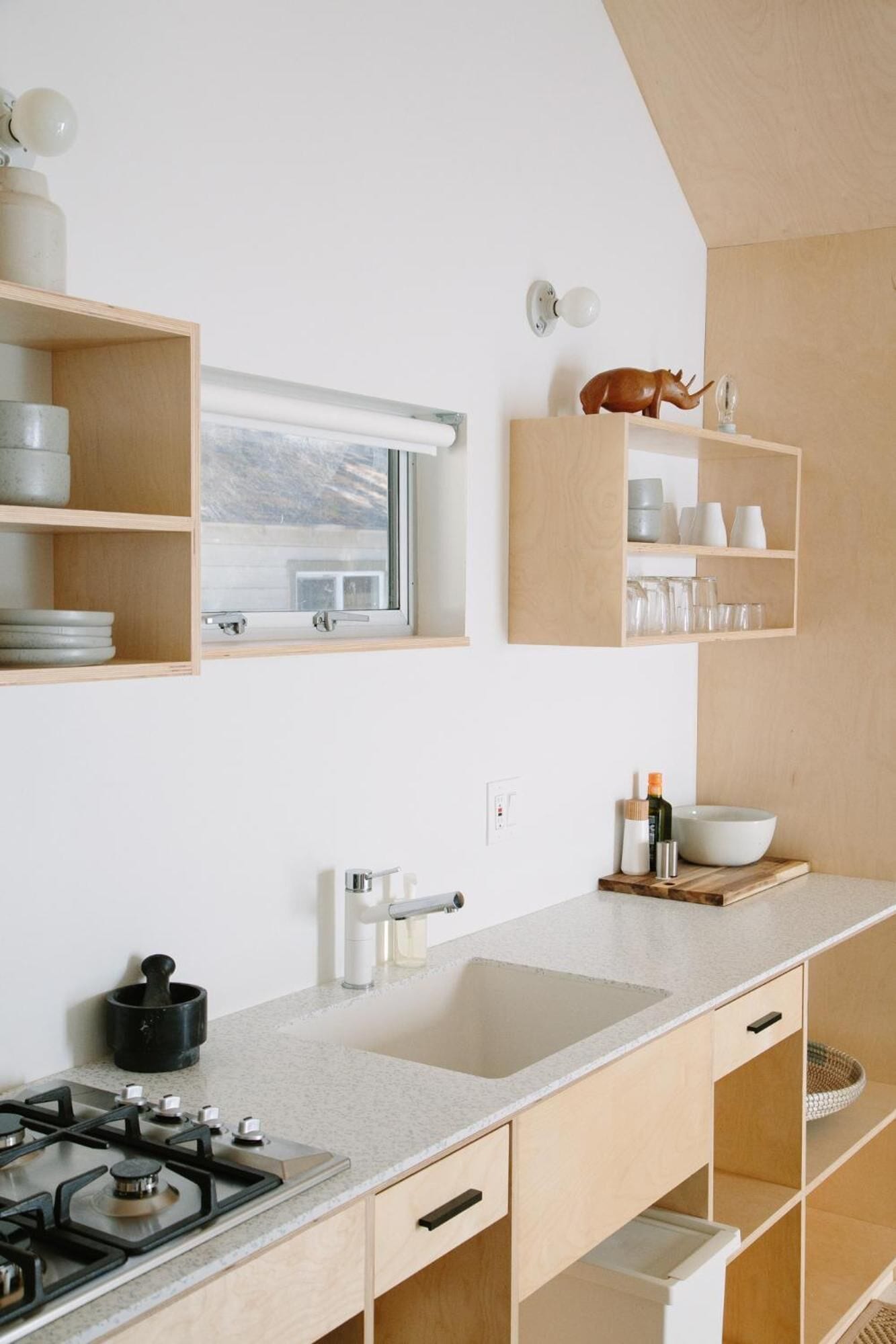 Una cocina moderna con estufa a gas, lavamanos, estanterías de madera y una ventana con vistas.