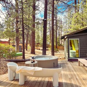 A hot tub on a wooden deck surrounded by tall trees, with a small building in the background. - Colorado Lodge (Big Bear Lake)