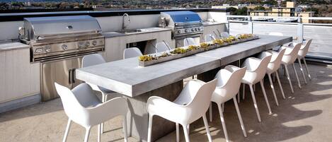 An outdoor kitchen with a grill, seating, and a view of the city.