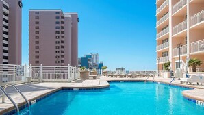 A swimming pool with a white fence, lounge chairs, and a view of tall buildings in the background. - Located in the Heart of Myrtle Beach, close to the Beach, Museum's, with access to all amenities (Myrtle Beach)