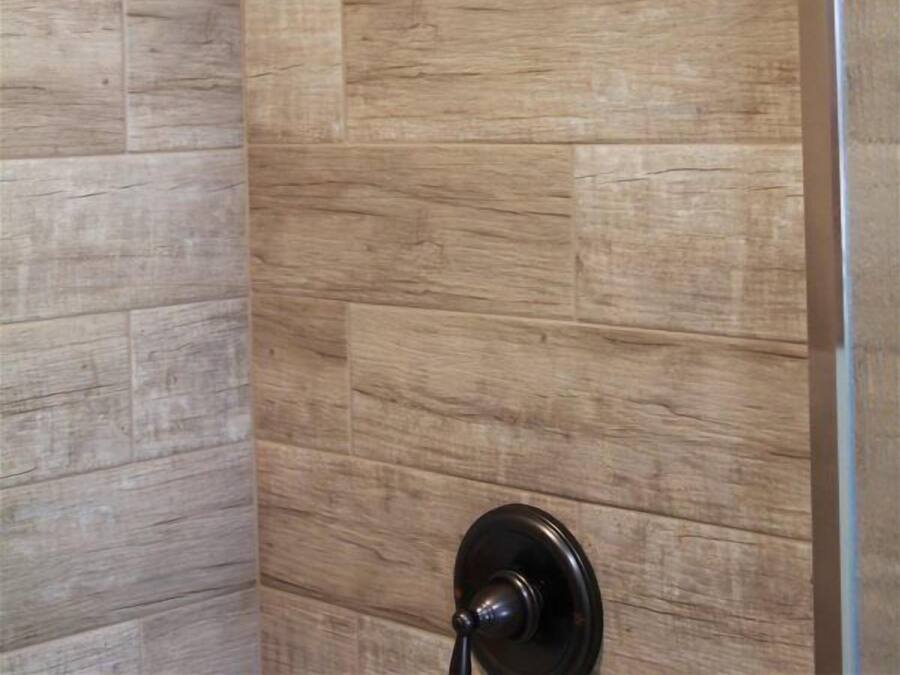 A shower with a wall-mounted rain showerhead and a door with a round handle.