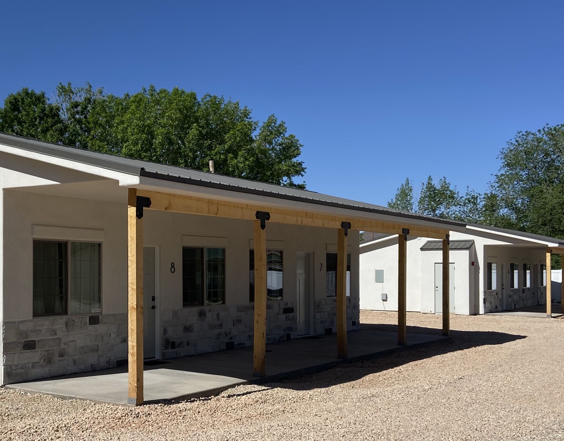 A row of single-story buildings with a covered outdoor area, numbered 7 and 8, surrounded by gravel and trees.