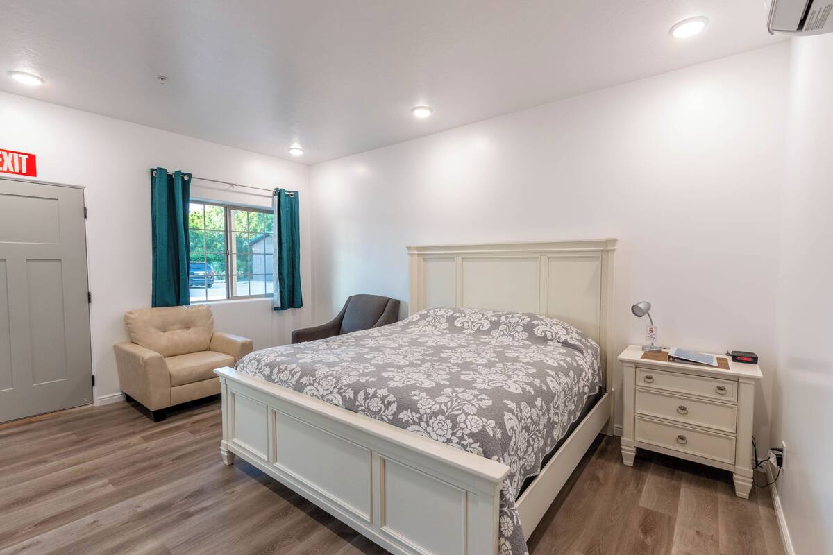 A bedroom with a bed, a chair, a nightstand, and a window with curtains.