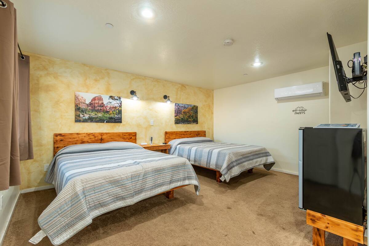 A room with two beds, a flat-screen TV, an air conditioner, and a painting on the wall.