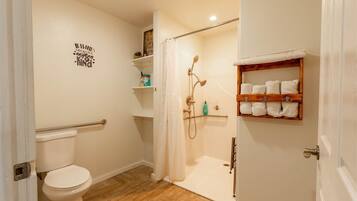 A bathroom with a toilet, shower, and a shelf with towels.