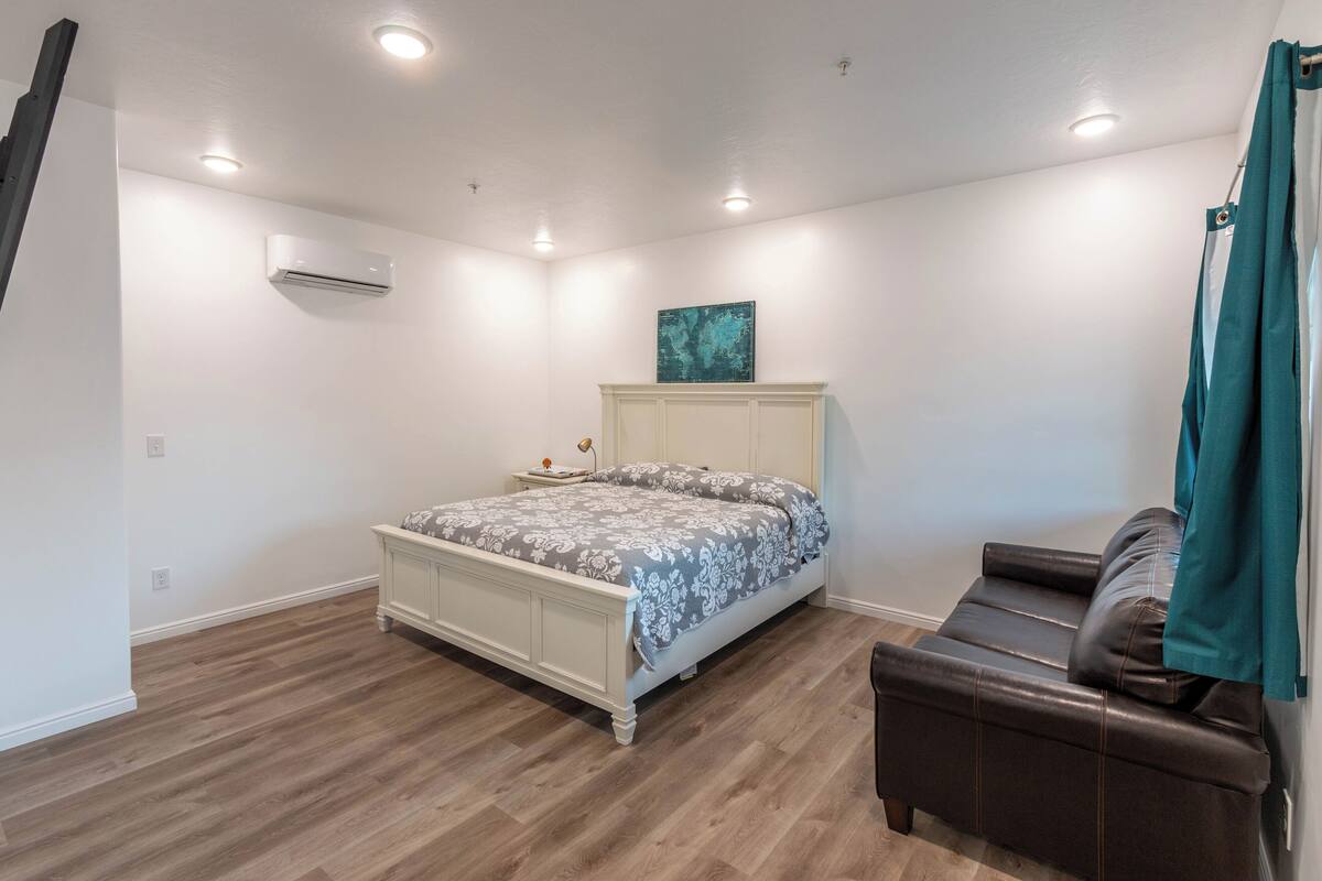 A bedroom with a bed, a nightstand, a dresser, a bench, and an air conditioning unit.