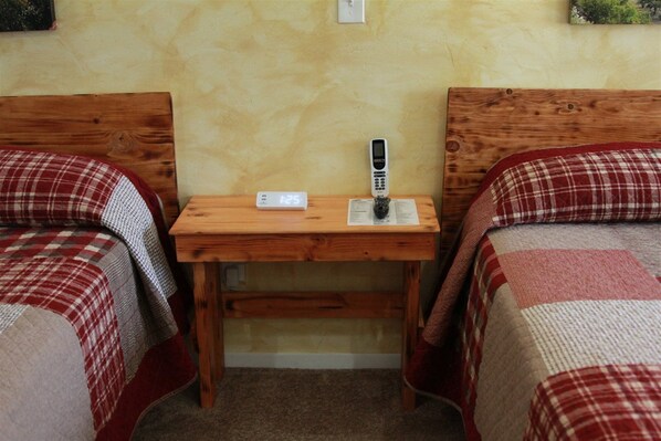 A small room with two beds, each with a red and white checkered blanket. There is a wooden table in the center with a clock and a remote control. - Hurricane Hideaway Lodging (Hurricane)